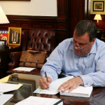 Christie at desk signing budget